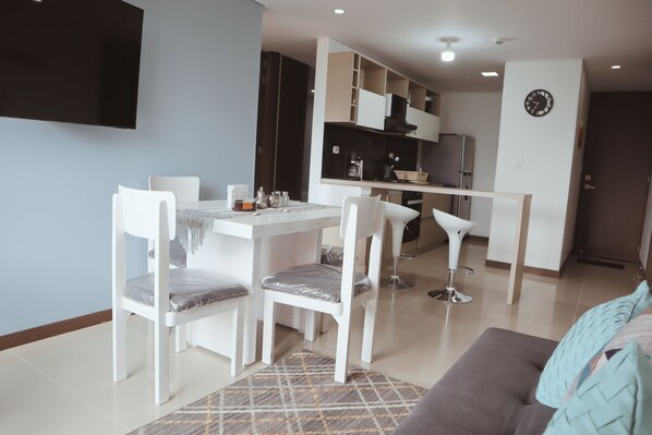 A modern living room with a dining area, a sofa, and a TV mounted on the wall.