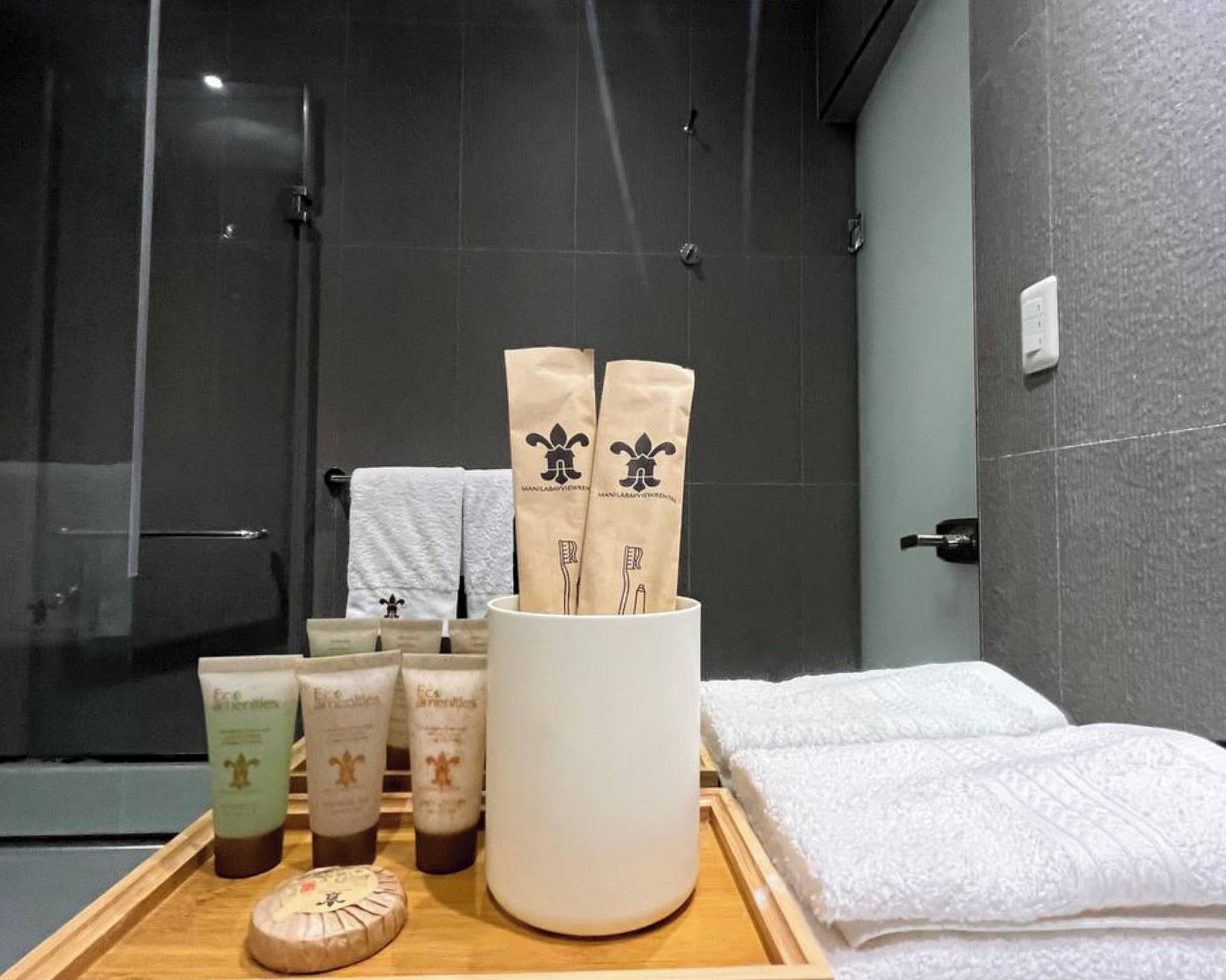 Un baño con ducha, un recipiente con artículos de aseo y toallas.