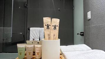 Un baño con ducha, un recipiente con artículos de aseo y toallas.