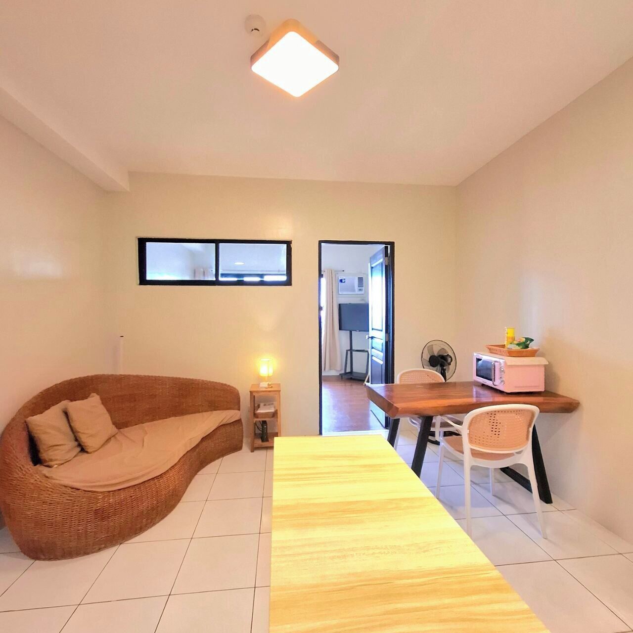 A modern living room with a curved sofa, a wooden dining table, and a small kitchen area with a microwave and fan.