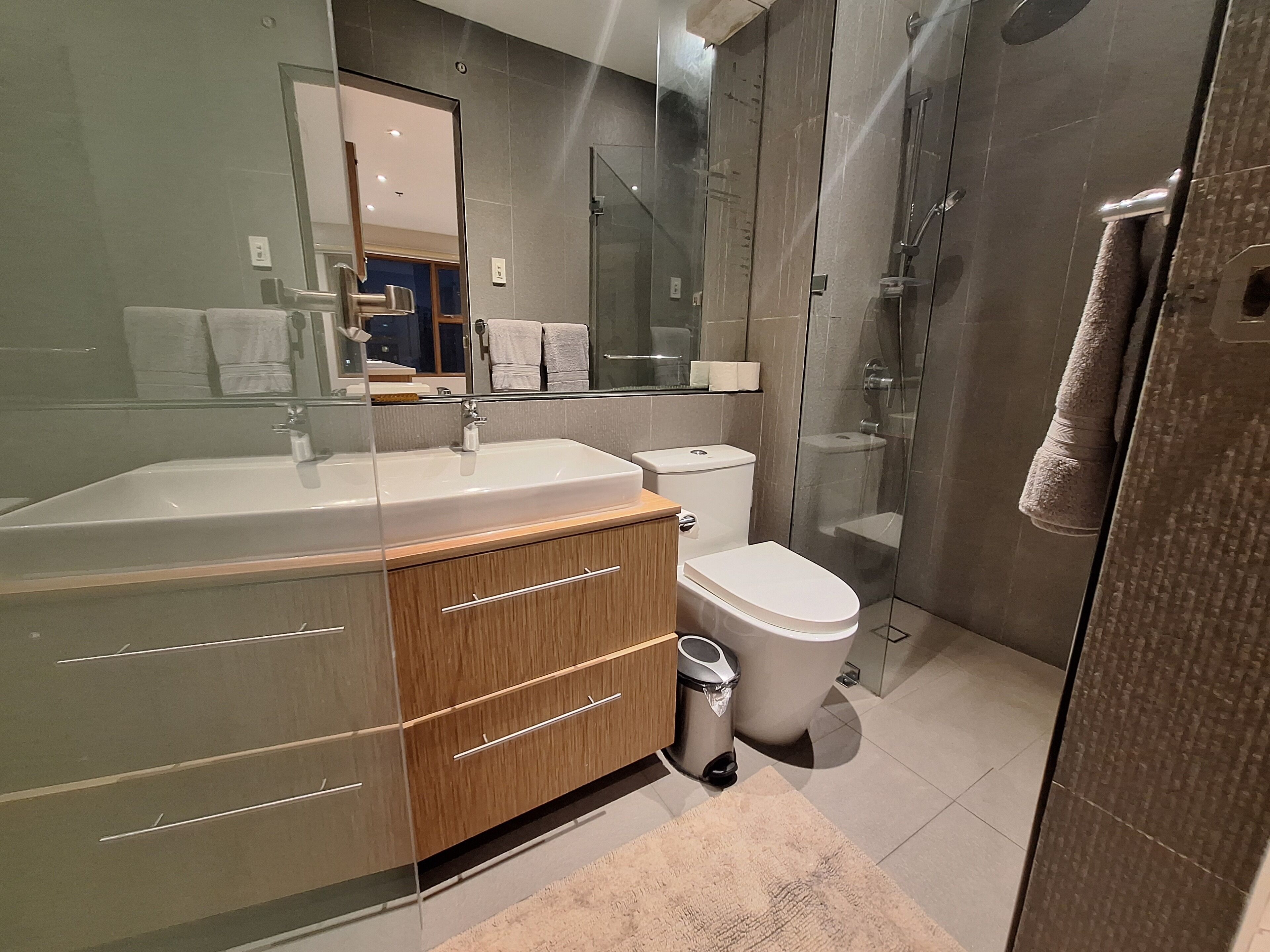 A modern bathroom with a glass-enclosed shower, a wooden vanity, and a large mirror.