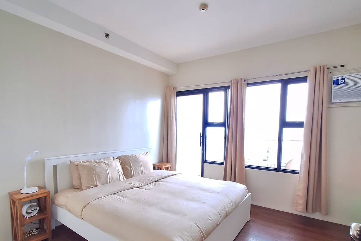 A bedroom with a bed, wooden nightstands, a ceiling light, and a window with curtains.