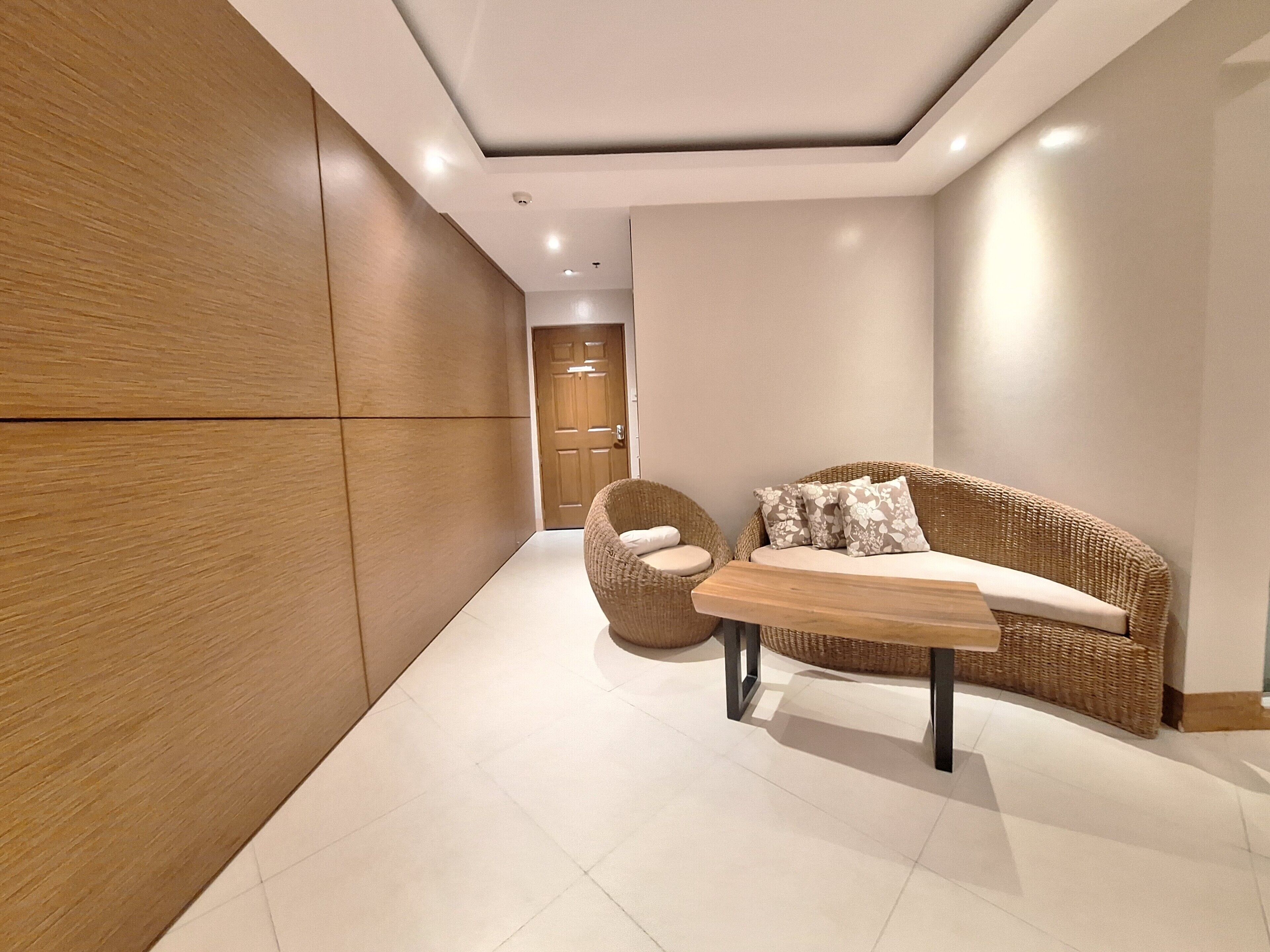 Un interior moderno con un panel de pared de madera, un sofá de mimbre con cojines estampados, una silla redonda de mimbre y una mesa de centro de madera.