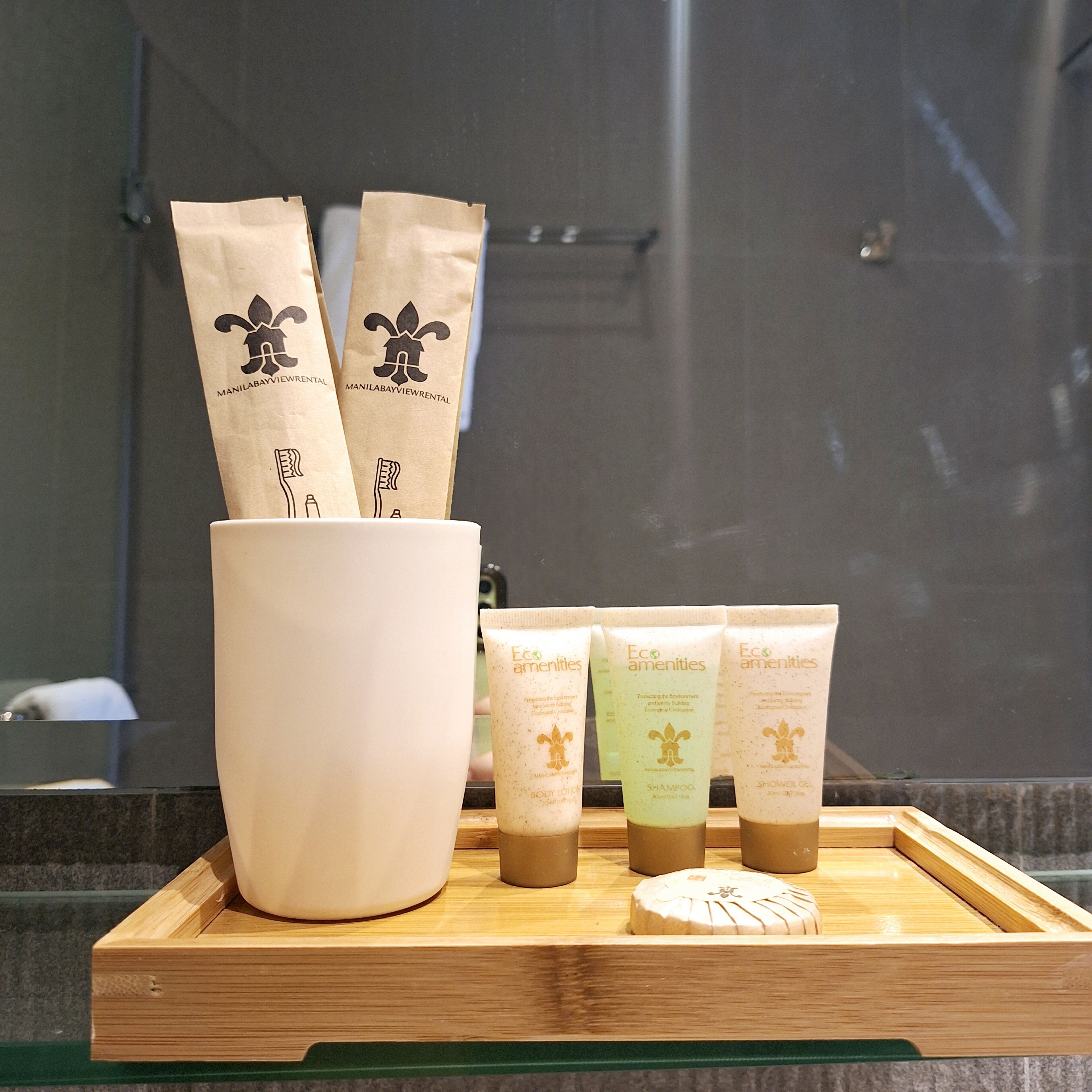A tray with toiletries including a large white mug, three brown paper bags, and three tubes of shampoo and body lotion.