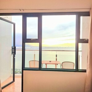A balcony with a table and chairs, overlooking a body of water and distant land.