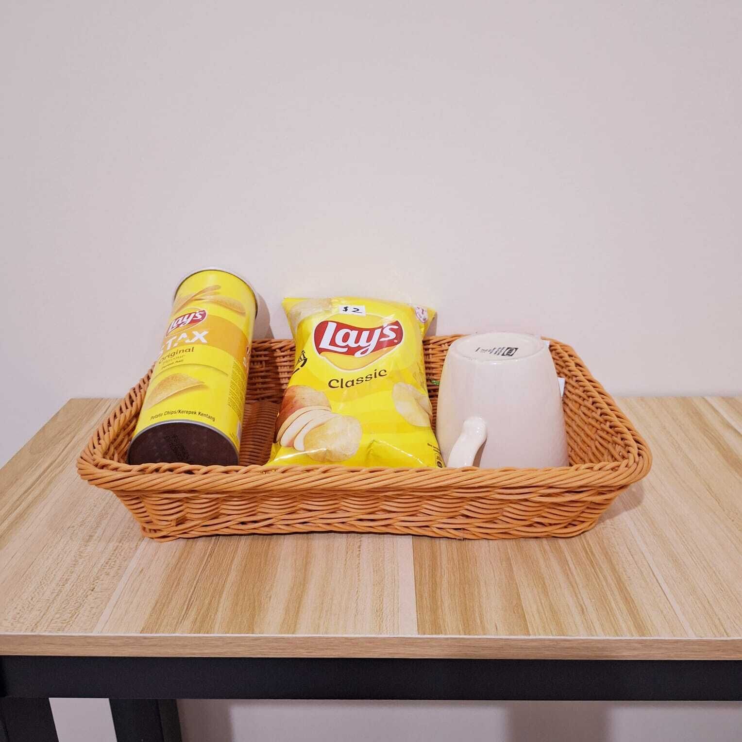 A wicker basket containing Lay's Classic potato chips, a can of Lay's Original potato chips, and a white mug on a wooden table.