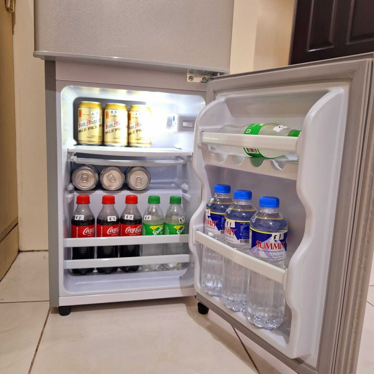 Un refrigerador con estantes llenos de bebidas, incluyendo cerveza, refrescos y agua.