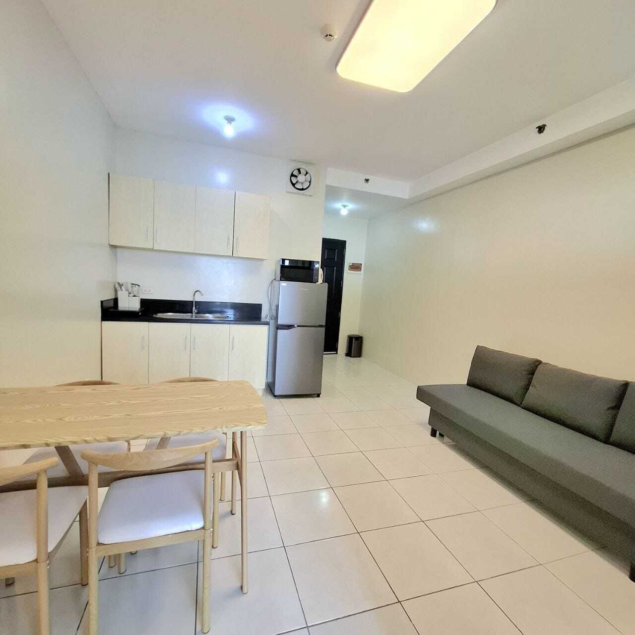A modern kitchen with white cabinets, a dining table with chairs, a refrigerator, and a grey sofa.