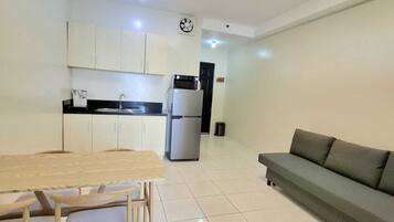 A modern kitchen with white cabinets, a dining table with chairs, a refrigerator, and a grey sofa.