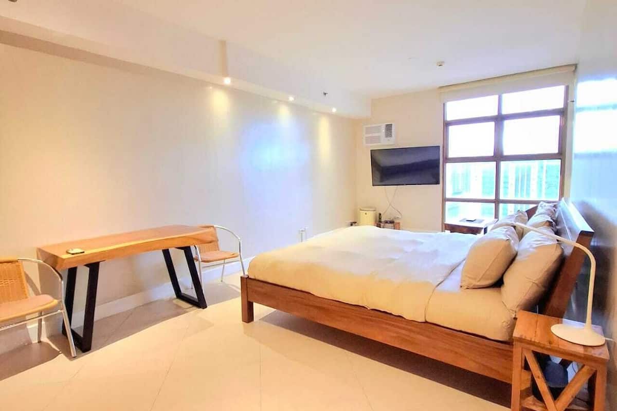 A modern hotel room with a large bed, a desk, a chair, and a TV mounted on the wall.