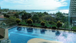 A swimming pool with a hot tub, surrounded by greenery and overlooking a body of water with buildings in the background. - StayLuxia Manilabayview (Manila)