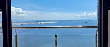 Un balcon avec une table et deux chaises, donnant sur une étendue d’eau et une côte lointaine.