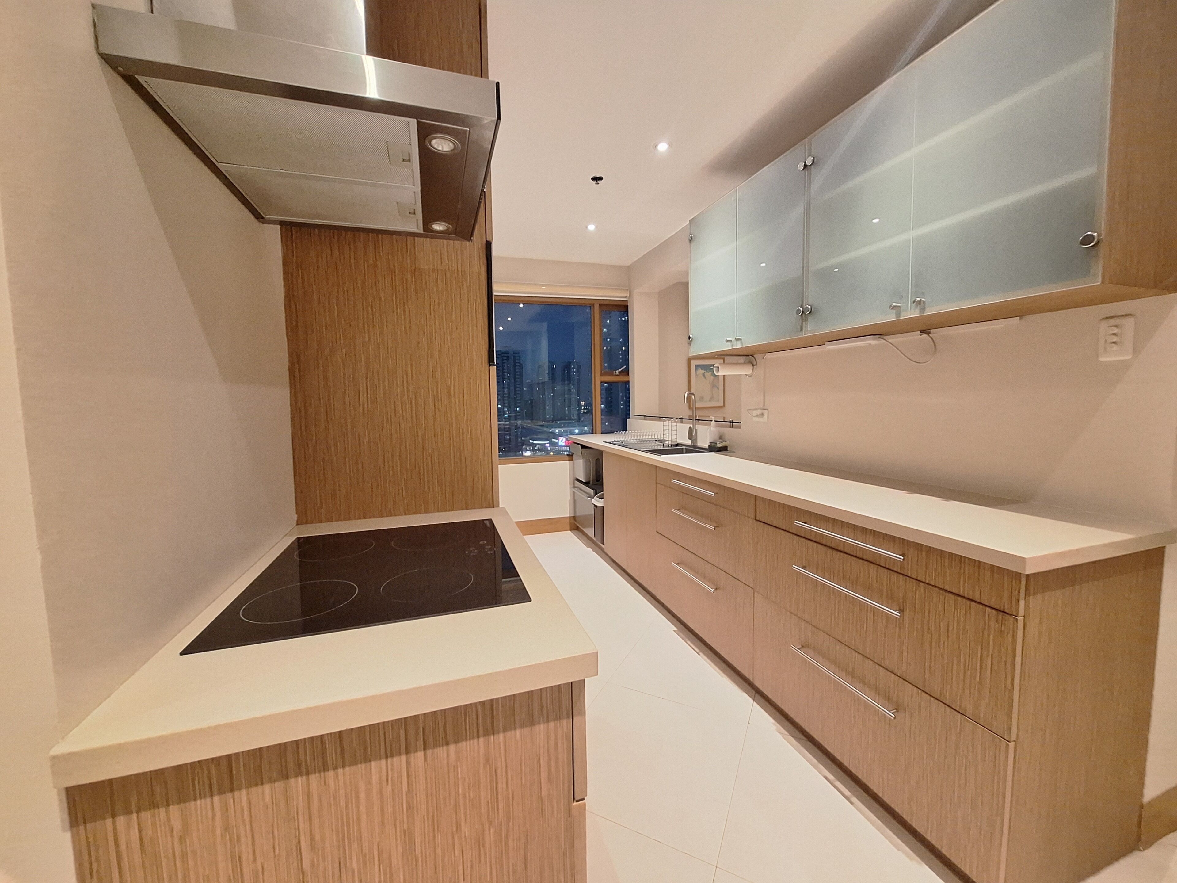 Una cocina moderna con estufa integrada, armarios de madera y vistas a la ciudad de noche.