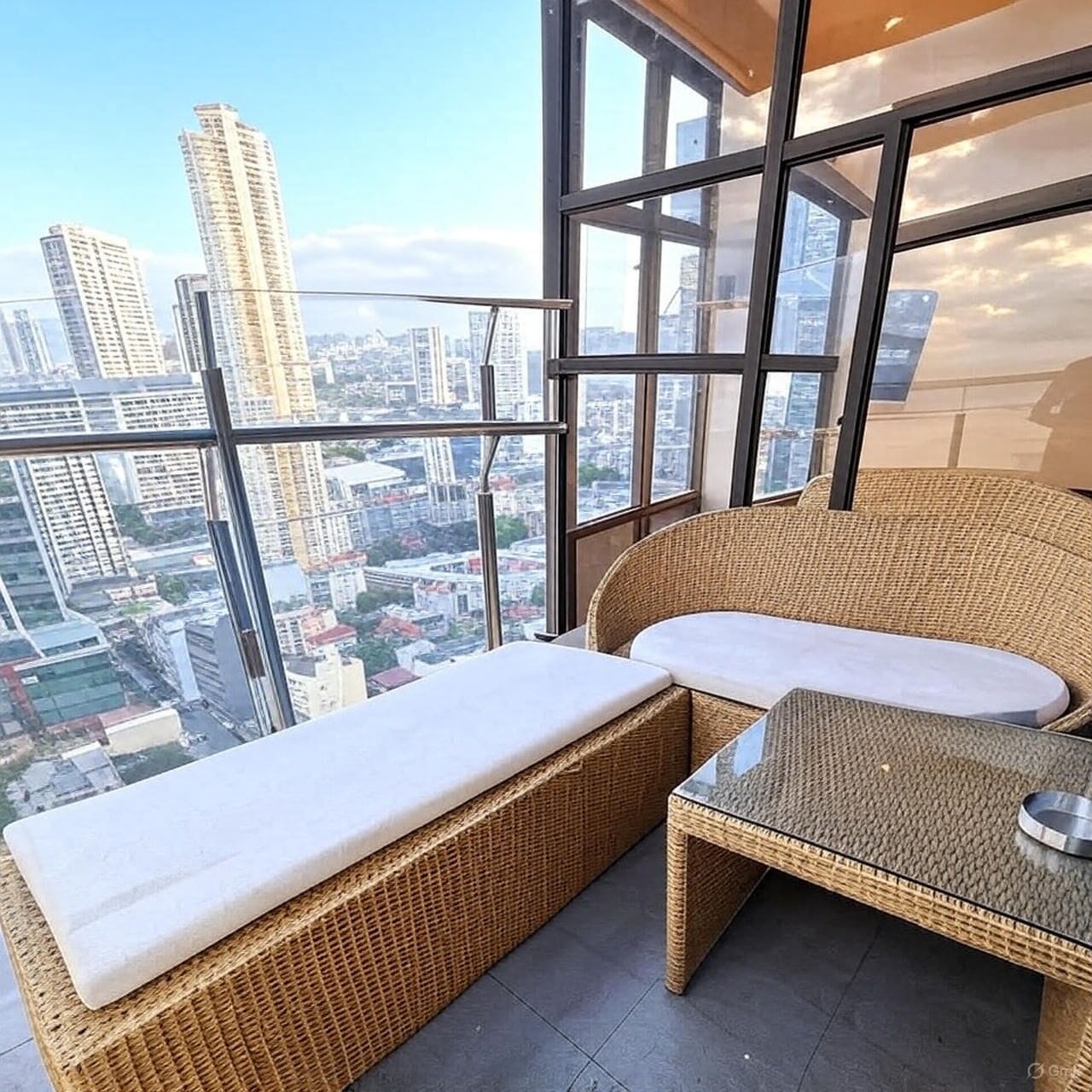 A balcony with wicker furniture, a glass table, and a city view.