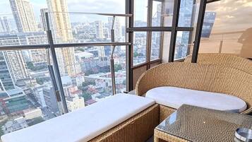 A balcony with wicker furniture, a glass table, and a city view.