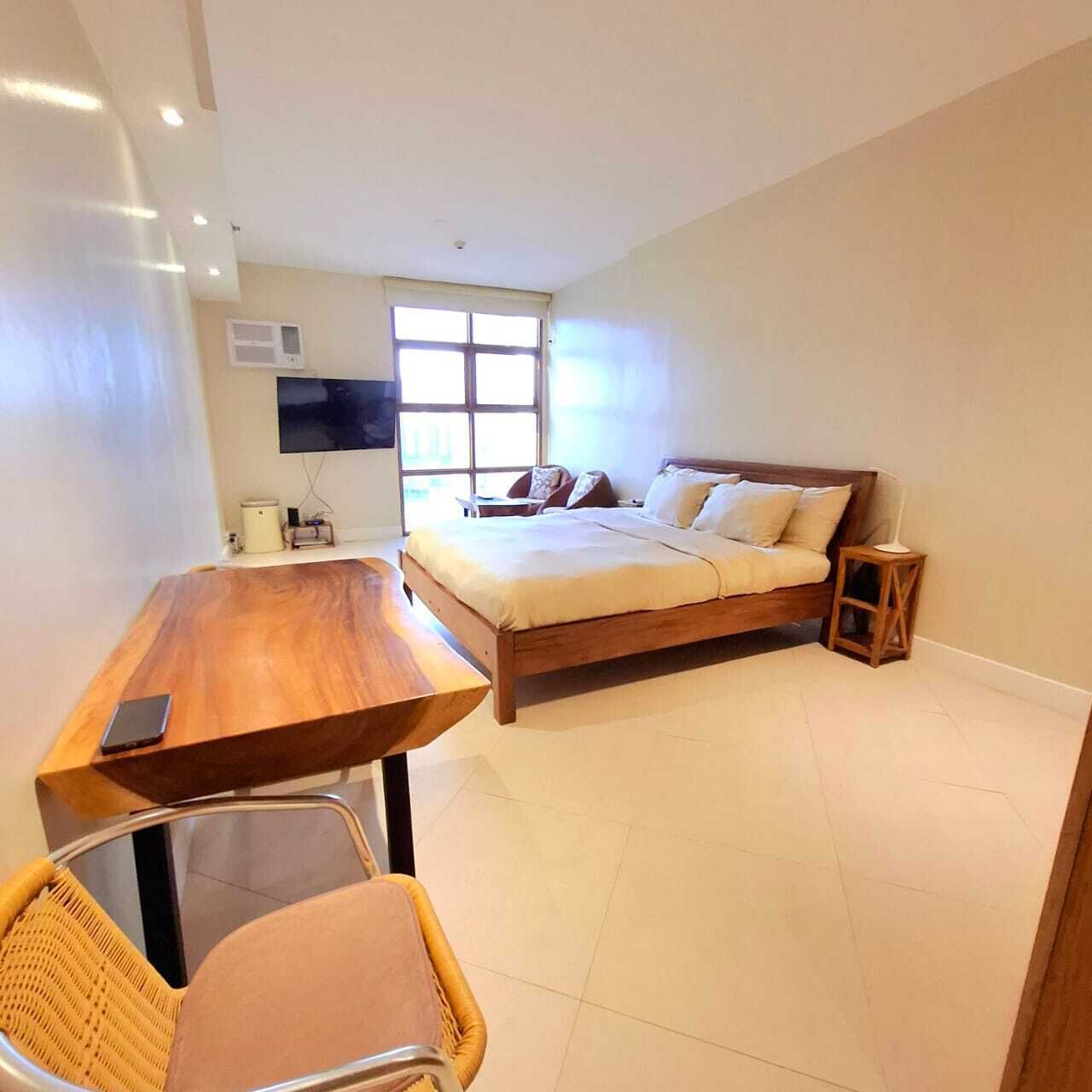 Une chambre à coucher avec un lit en bois, une petite table de chevet, une chaise, un bureau et un téléviseur fixé au mur.