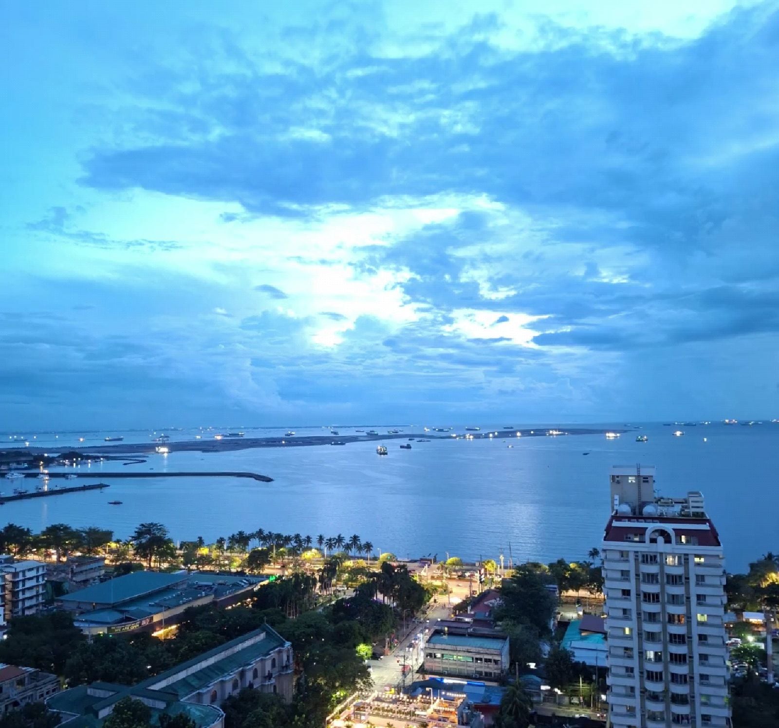 Paisagem costeira com vista para o mar, edifícios e um hotel de design moderno em destaque.