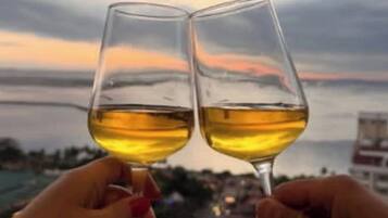 Deux mains tenant des verres à vin, avec un coucher de soleil en arrière-plan.