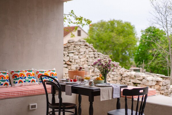 An outdoor dining area with a stone wall backdrop, a table set with plates, glasses, and a vase of flowers. - Villa Imagination with Pool (Gornji Humac)