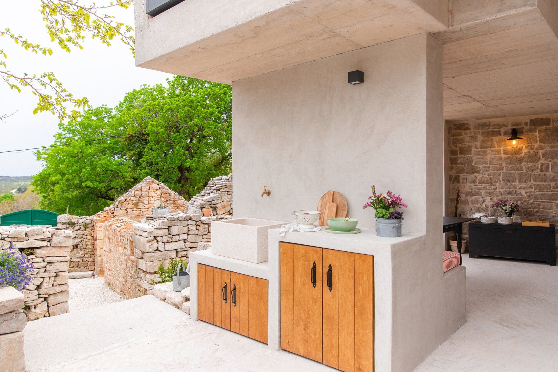 An outdoor kitchen area with a stone wall, wooden cabinets, and a sink.