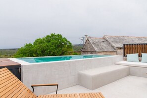 A rooftop infinity pool with a view of the countryside, a wooden deck, and a stone building with a tiled roof. - Villa Imagination with Pool (Gornji Humac)