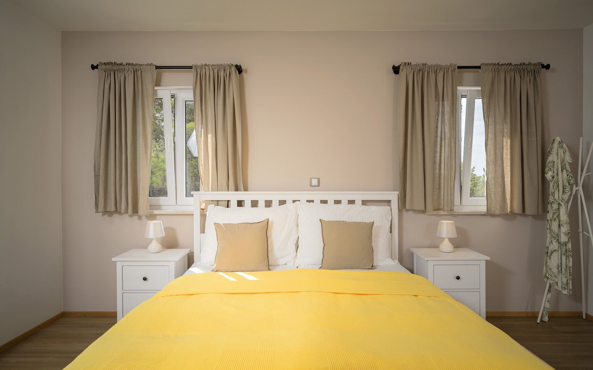 Un dormitorio con una cama, dos mesitas de noche, una ventana con cortinas y una mesilla con lámpara.
