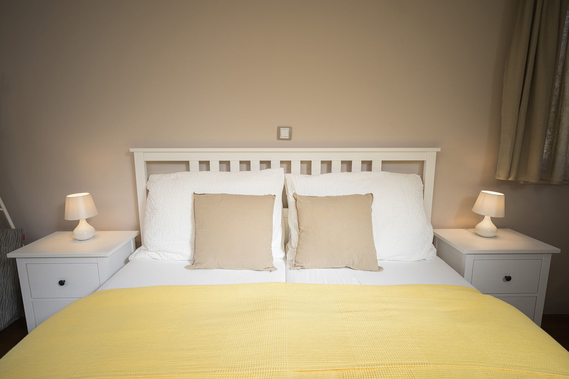 Uma cama com cabeceira branca, duas mesas de cabeceira com abajures e um edredom amarelo.