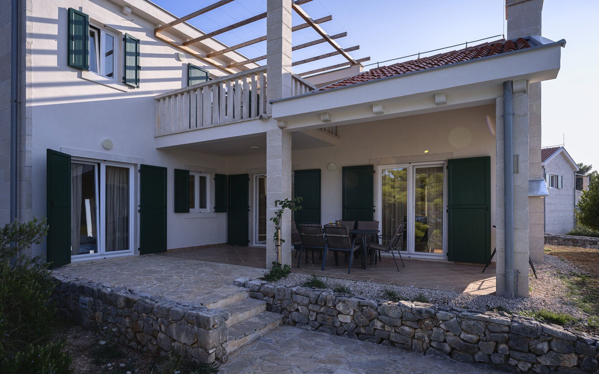 A two-story house with a covered patio, stone steps, and a view of the surrounding area.