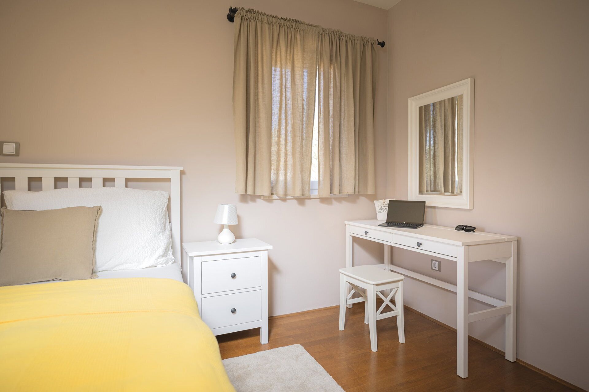 A bedroom with a bed, bedside table, desk, chair, and a laptop.