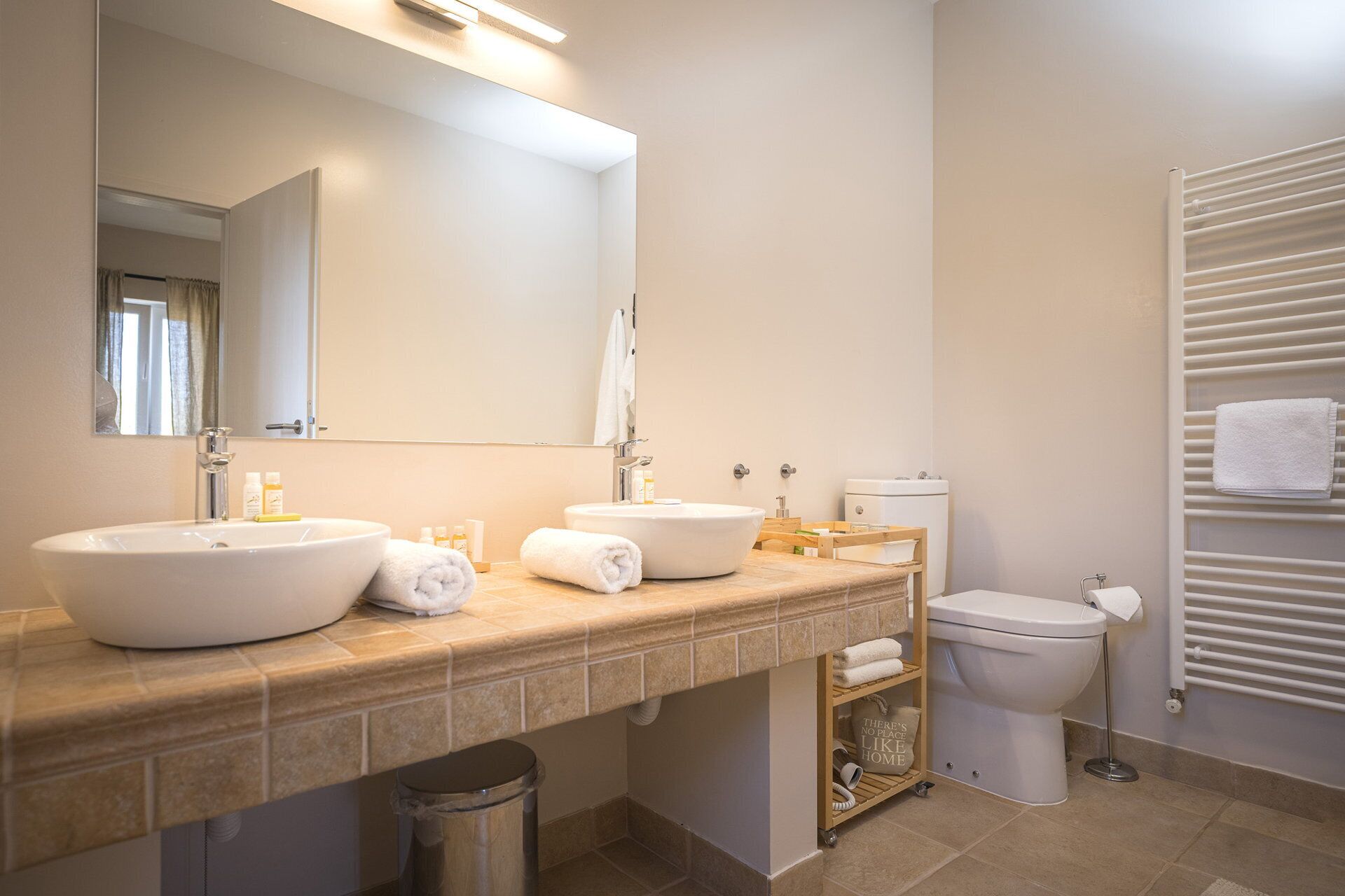 A modern bathroom with a large mirror, two sinks, a toilet, and a towel rack.