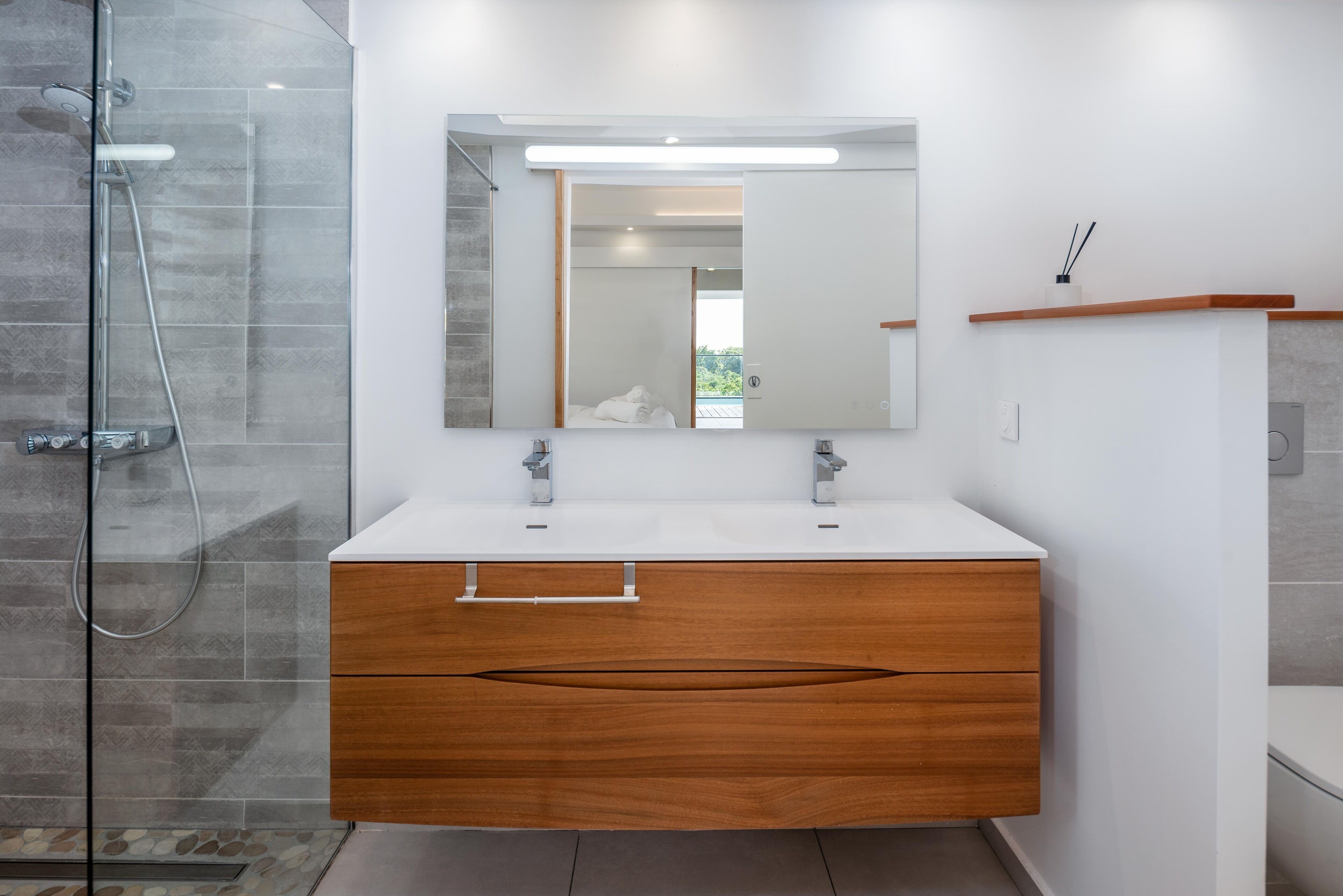 A modern bathroom with a glass shower enclosure, a white vanity with a wooden cabinet, and a large mirror above the vanity.