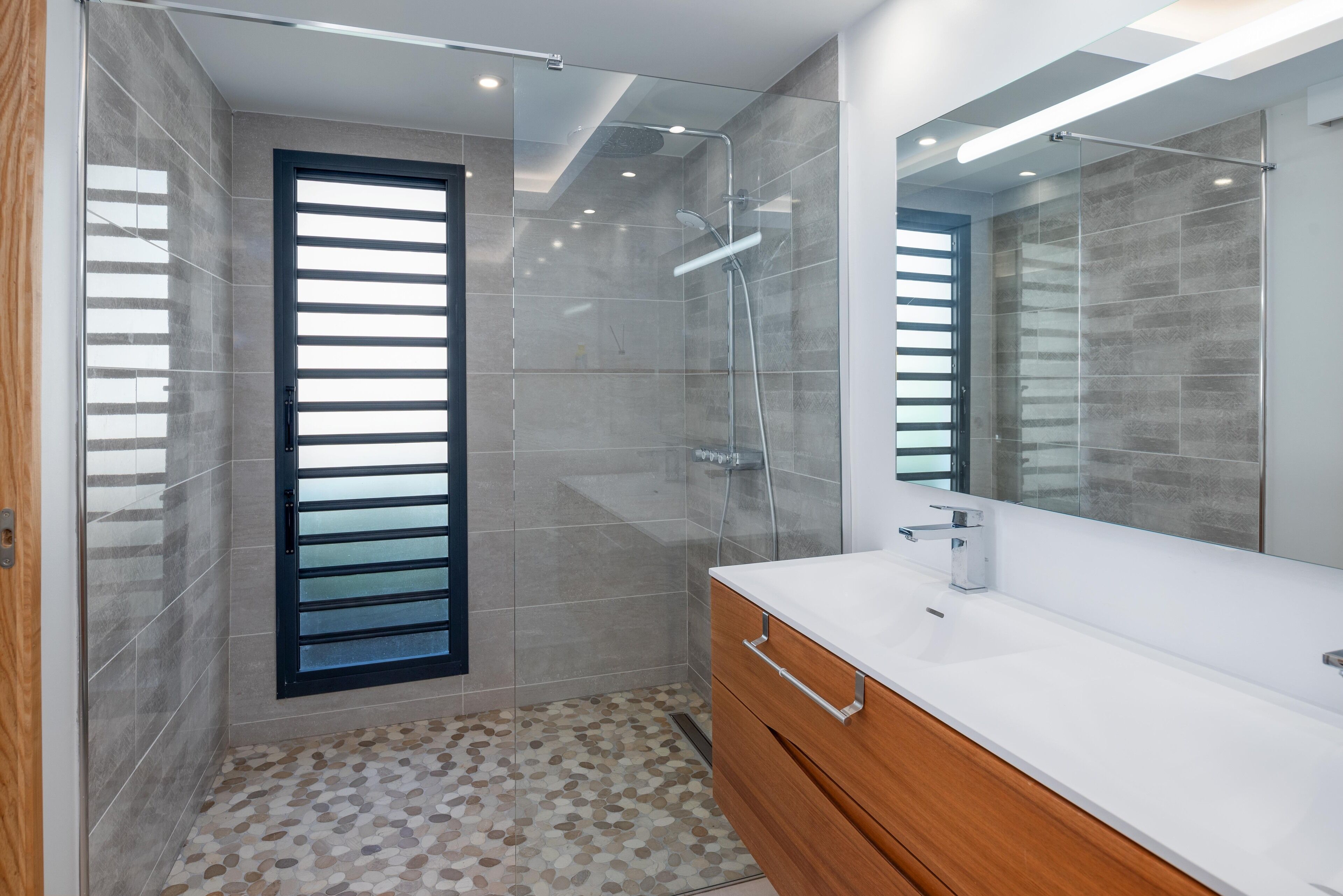 A modern bathroom with a shower, a large mirror, and a vanity with a sink.