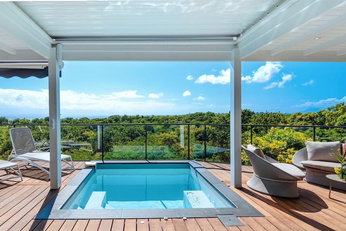 A poolside area with a view of the ocean, a covered seating area, and a table with chairs.