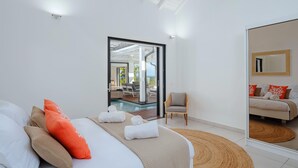 A modern hotel room with a large bed, a view of the outdoor pool, and a seating area with a chair and a sofa. - Vista del Mar (Sainte-Anne)