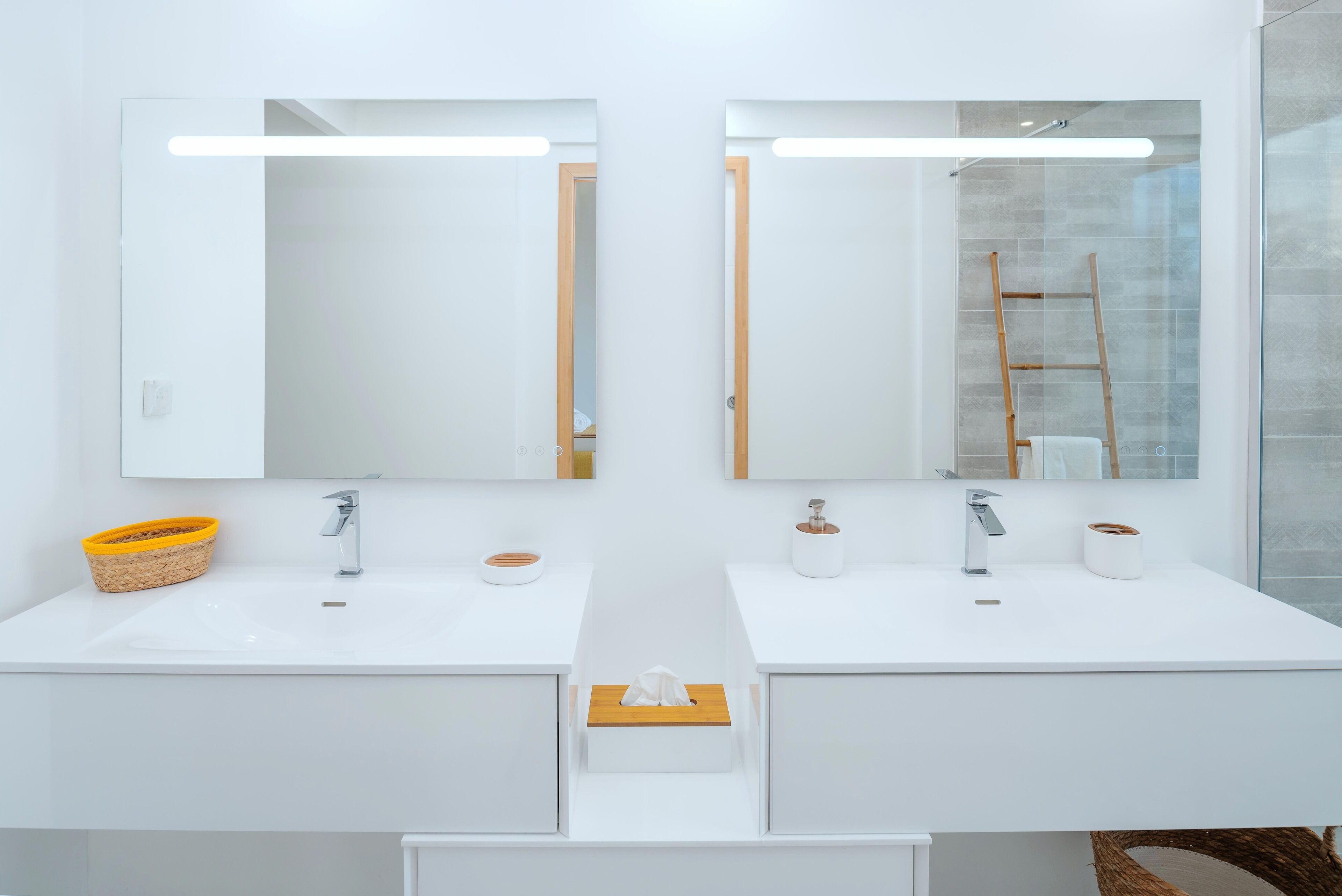 A modern bathroom with two sinks, each with a mirror above. There is a towel rack on the left and a wooden ladder in the shower area.