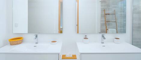 A modern bathroom with two sinks, each with a mirror above. There is a towel rack on the left and a wooden ladder in the shower area.