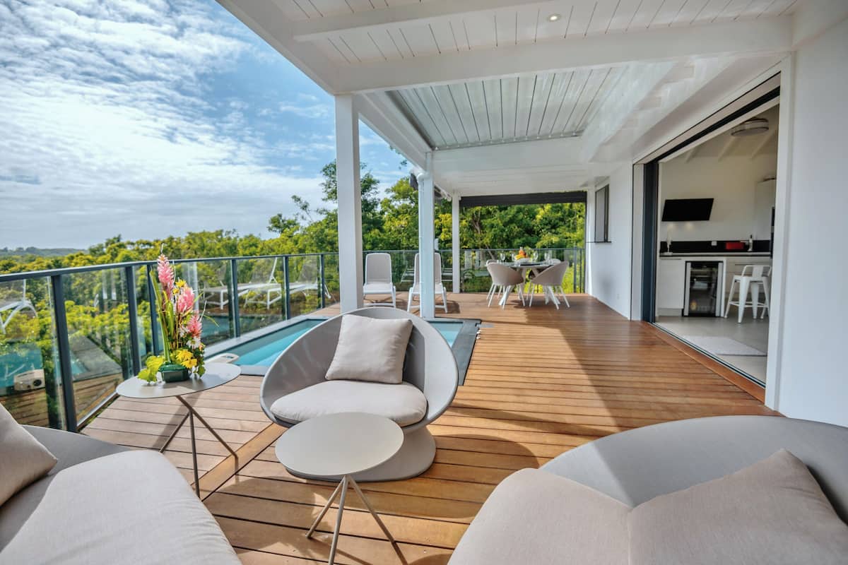 A modern outdoor deck with a pool, seating, and a kitchen area.
