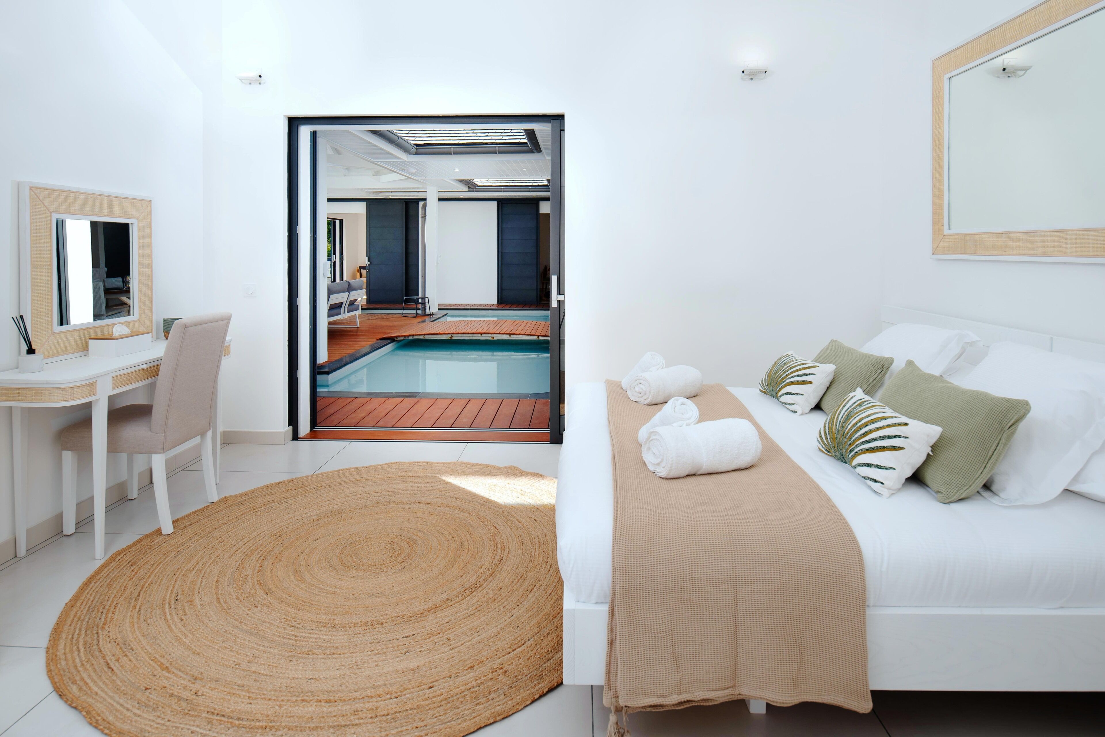 A modern hotel room with a large bed, a desk, a chair, and a view of a swimming pool.