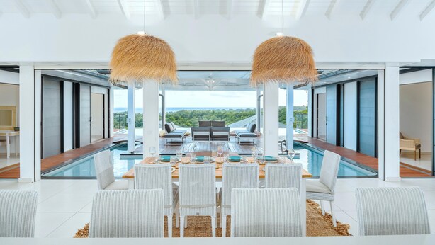 A modern dining area with a pool view, white wicker furniture, and a large glass table. - Vista del Mar (Sainte-Anne)