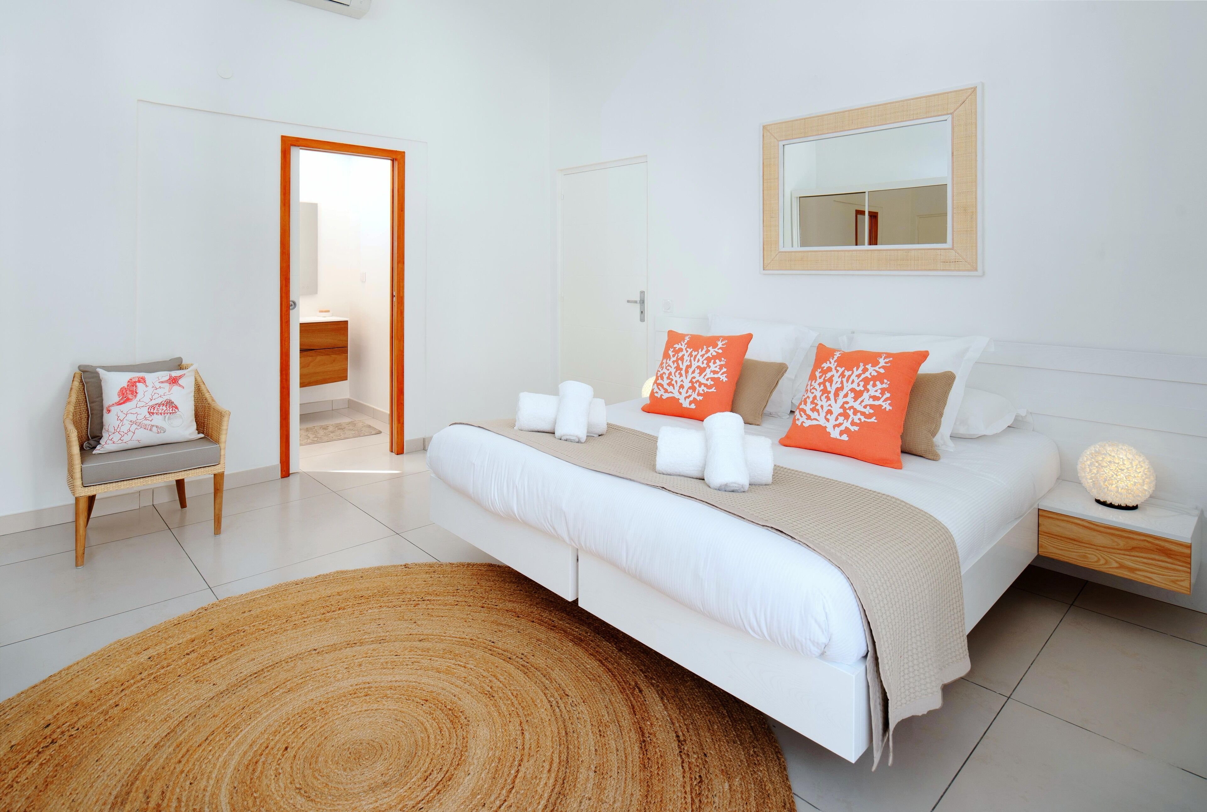 A modern bedroom with a large bed, a bedside table with a lamp, a chair, and a mirror on the wall.
