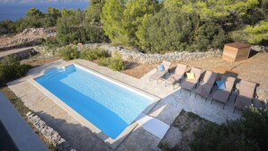 A rectangular swimming pool with a stone border, surrounded by lounge chairs and a wooden deck. - Villa Pharia with Pool VIII (Stari Grad)
