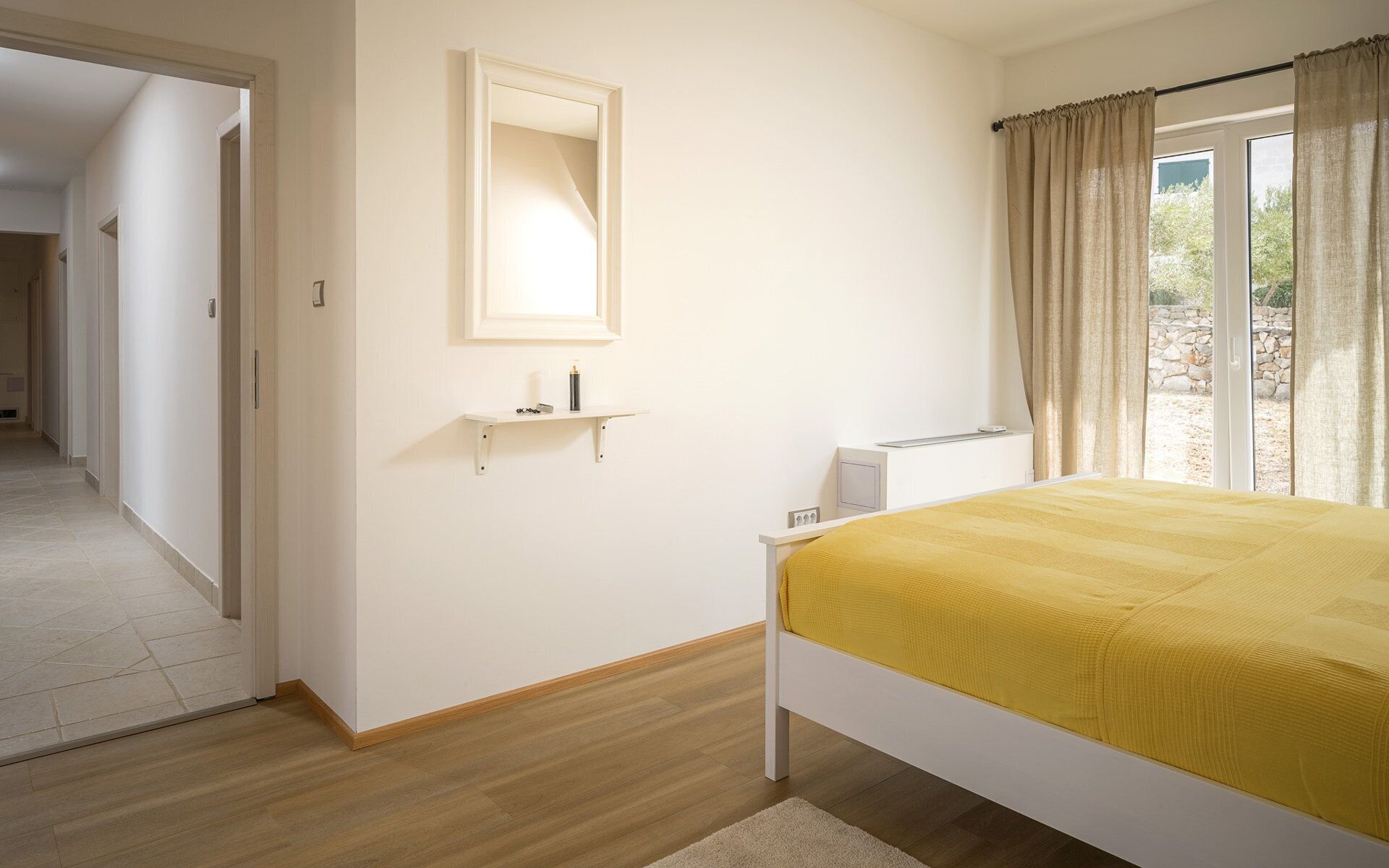 Un dormitorio con cama, mesita de noche, espejo y ventana con cortinas.