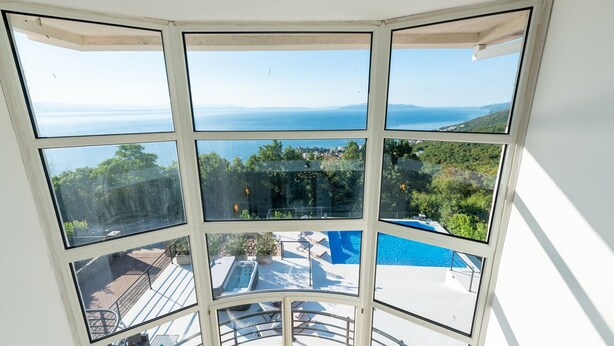 A corner room with a large bay window overlooking a pool and a scenic view of the sea. - Villa Piano with Pool (Matulji)