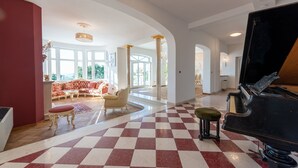 A spacious living area with a grand piano, a red and white checkered floor, and a large window offering a view of the outdoors. - Villa Piano with Pool (Matulji)