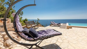A sun lounger with a view of the sea, a wooden bench, and a pool.