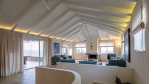 A spacious living area with a high ceiling, a fireplace, and a view of the sea.