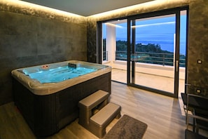 Ein modernes Badezimmer mit Whirlpool, einer großen Schiebeglastür, die auf einen Balkon führt, und Blick ins Freie.