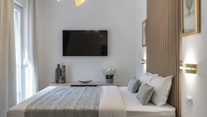 A modern hotel room with a large bed, a flat-screen TV mounted on the wall, a bedside table with decorative items, and a nightstand with a lamp.