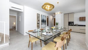 A modern dining room with a glass table, wooden chairs, and a contemporary pendant light.
