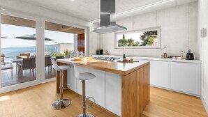 Une cuisine moderne dotée d’un grand îlot central, de tabourets de bar et offrant une vue sur l’extérieur.